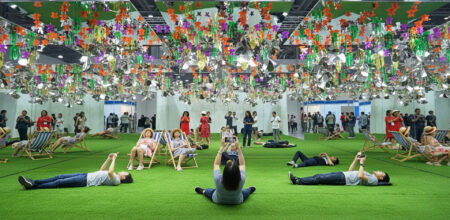vista di un'installazione in uno spazio con moquette verde e supporti decorati sospesi